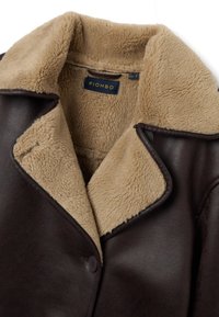 Abrigo de cuero marrón con un forro peludo color marrón claro. Presenta un cuello ancho, botones y un acabado texturizado, mostrando un diseño cálido y acogedor.