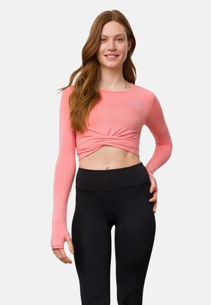 Rosa langärmliges Crop-Top mit einem verdrehten Vorderteil, kombiniert mit hochgeschnittenen schwarzen Leggings. Glatte Textur, taillierte Passform.