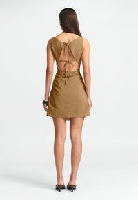 Pruun kleit tagumise lõikeava, reguleeritava sidumisega ja tekstuurse kangaga. Suvekleit, millel on varrukateta disain ja A-line kuju, ulatudes keskmise reieni.