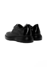 Zapatos de cuero negro con una textura suave, punta redondeada, tirador trasero y suela gruesa de goma con un sutil patrón de relieve.