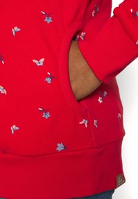 Czerwona bluza z haftowanymi wzorami kwiatowymi i motylami w kolorach niebieskim i różowym. Ze ściągaczami na mankietach i dole oraz boczną kieszenią.