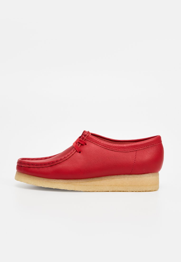 Red leather shoe with a rounded toe, featuring a stitched design and lace-up closure. It has a light beige, textured rubber sole.
