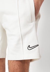 White athletic shorts made of soft fabric with a textured surface. Features side pockets and a black embroidered Nike logo on the hem.