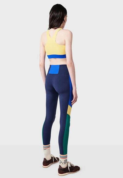 Sportbh i gult och blått, pairad med marinblå leggings med flerfärgade paneler och randiga strumpor. Mjuk, stretchig material genom hela.