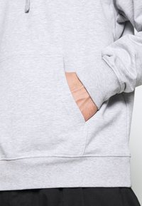 Felpa grigia chiara con tasca a marsupio, polsini a costine e una texture morbida. Il design è informale con una vestibilità rilassata.