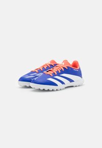 Bottes de football synthétiques bleues avec des rayures blanches et des lacets orange vif. Elles possèdent une tige texturée et une semelle blanche avec des crampons de traction.