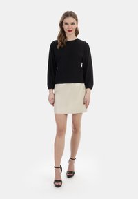 Sort langærmet top med rund halsudskæring, parret med en beige mini-nederdel. Sættet fuldendes af sorte højhælede sandaler.