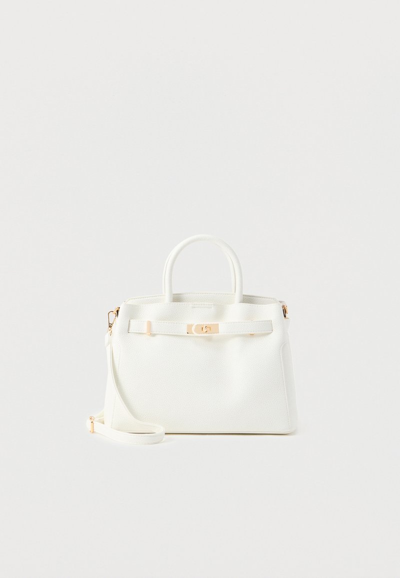 Λευκή υφασμάτινη χειραποσκευή με επάνω λαβές, χρυσό κούμπωμα και αφαιρούμενο ιμάντα ώμου σε απλό φωτεινό φόντο.