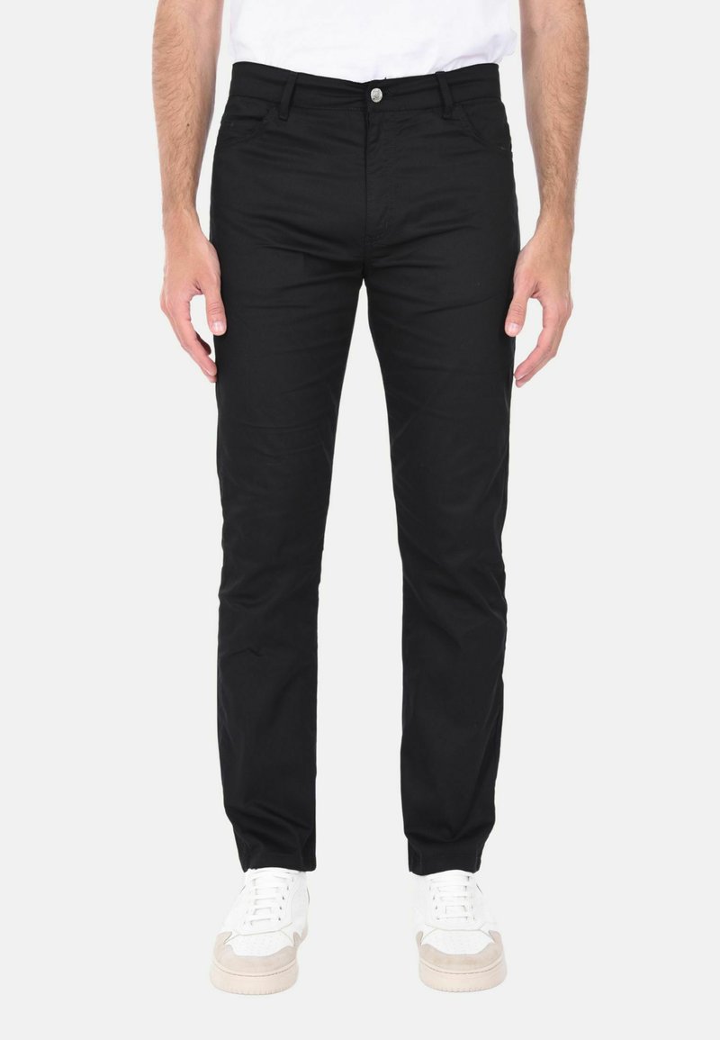 Pantaloni neri con un design aderente, realizzati in tessuto elasticizzato, dotati di chiusura frontale con bottone e tasche laterali, abbinati a sneakers bianche.