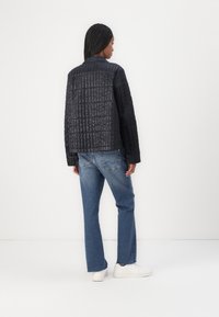 Quiltad svart jacka med en texturerad yta, avslappnad passform, sänkta axlar, kombinerad med ljusblå denimjeans och vita sneakers.