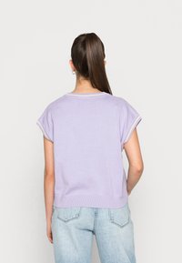 Ljubičasti kratki rukav s okruglim izrezom i rebrastim rubom. Ima kontrastne svijetle rubove uz rukave. Nosiv s svijetloplavim trapericama.