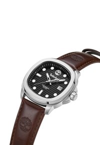 Timberland kvadratna ura s črnim strukturiranim številčnicom, srebrnim okvirjem, belimi oznakami ur in rjavim usnjeni paščkom z embosiranim logotipom.