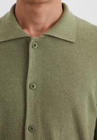 Green textured polo shirt with a collared neckline, featuring three buttons and a soft, woven fabric.