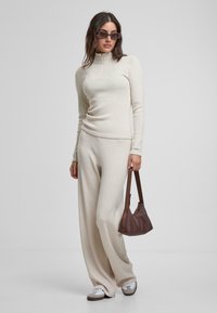 Beige strikket turtleneck og vide bukser, med et teksturert stoff. Tilbehøret inkluderer mørke solbriller og en brun skulderveske.