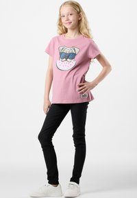 T-shirt in cotone rosa con una grafica di un cane che indossa occhiali da sole su una fetta di anguria. Abbinata a jeans neri slim-fit e sneakers bianche.