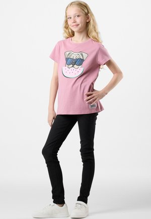 Rosa Baumwoll-T-Shirt mit einem Grafikdesign eines Hundes in Sonnenbrille auf einer Wassermelonen-Scheibe. Kombiniert mit schwarzen Slim-Fit-Jeans und weißen Sneakern.