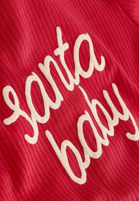 Rød stof med ribbet tekstur og hvid kursiv skrift, der siger "santa baby." Designet fremhæver et legende og festligt tema.
