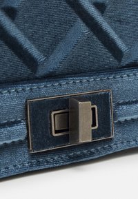 Texturerad mörkblå tygpåse med en platt rektangulär metallspänne. Ytan har ett diamantmönster med en slät finish.