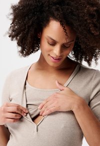 Beige geripptes Shirt mit V-Ausschnitt und Druckknopfverschluss, darüber getragen ein passendes Tanktop. Verfügt über kurze Ärmel und eine weiche Textur.