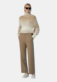 Flauschiger beiger Pullover mit Rollkragen, kombiniert mit hellbrauner Hose und weißen Sneakers. Glatte Textur, lässiger Schnitt und minimale Akzente.