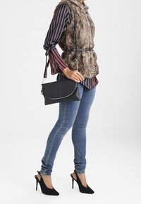 Borsa a spalla nera con superficie testurizzata, hardware argentato e patta arrotondata. Indossata con un gilet in pelliccia sintetica e jeans, con una silhouette slim.