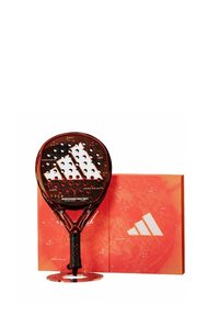 Adidas padel racket with a transparent red frame, perforated surface, and a black grip, displayed on a circular stand next to a red box.