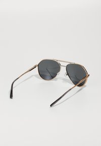 Óculos de sol com lentes cinzentas, armação metálica e detalhes em dourado. Apresenta uma ponte dupla e hastes pretas com um acabamento suave.