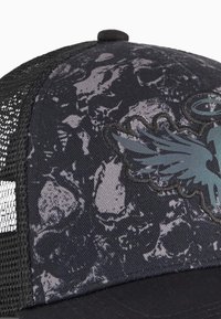 Sort trucker cap med mesh bag, struktureret mønster og broderet ørnedesign i grå og teal på frontpanelet.
