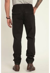 Pantaloni jogger neri con vita elasticizzata e cordino, polsini elasticizzati e due tasche posteriori, realizzati in tessuto di cotone con una texture liscia.