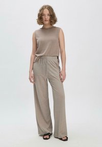 Beige ärmelloses Oberteil mit gerippter Textur, kombiniert mit hellbeigen weit geschnittenen Hosen mit elastischem Bund und Kordelzug. Schwarze Sandalen.