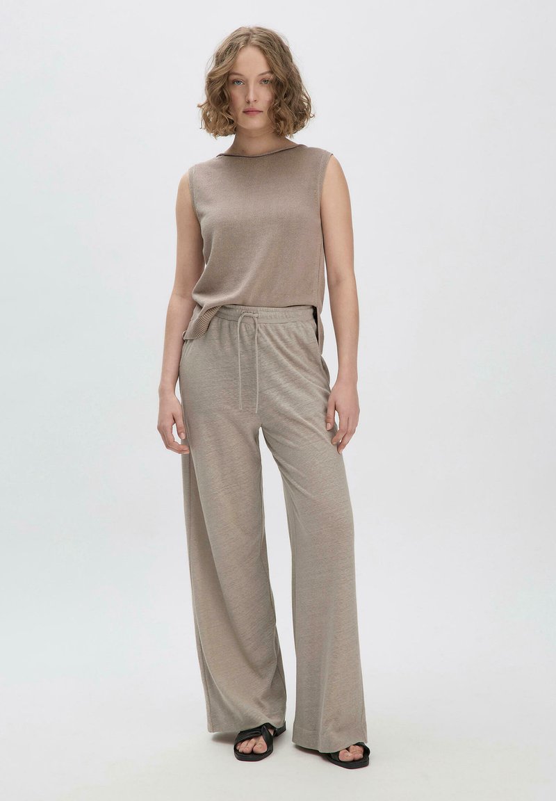 Beige ärmelloses Oberteil mit gerippter Textur, kombiniert mit hellbeigen weit geschnittenen Hosen mit elastischem Bund und Kordelzug. Schwarze Sandalen.