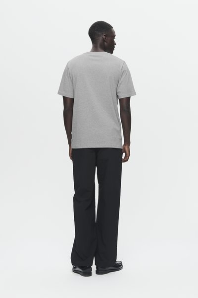 Gray short-sleeve t-shirt with a crew neck and a relaxed fit, worn with black loose-fitting pants and black shoes. Simple and minimalist design.