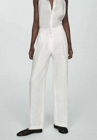 Pantaloni albi din in cu picioare largi și pliseuri frontale, asociați cu o bluză ușoară din in, fără mâneci, cu decolteu butonat.