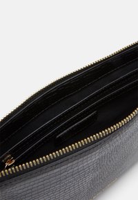 Černá kožená kabelka se strukturovaným povrchem a zlatým zipem, částečně otevřená, ukazující černou látkovou podšívku a zipovou kapsu uvnitř.