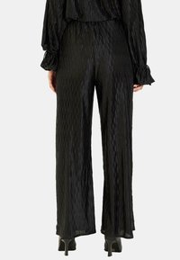 Czarne, plisowane spodnie o szerokich nogawkach z teksturowanym wykończeniem, z wysokim stanem i kontrastującym gładkim materiałem na końcach nogawek.