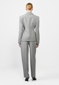 Szürke, testre szabott öltöny, amely magába foglal egy jól illeszkedő blézert széles vállakkal, egyhátsó szellőzőnyílással és egyenes szárú nadrággal, hegyes sarkú cipővel párosítva.