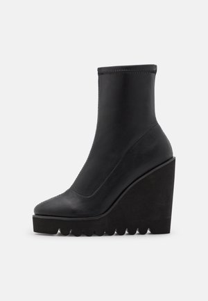 Bottes chevilles en cuir noir avec un talon compensé haut et une semelle texturée. Tige lisse avec un bout arrondi et des détails cousus.