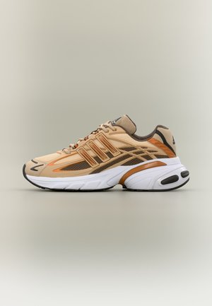 Zapatilla deportiva beige y marrón con suela blanca acolchada, paneles de malla transpirables y cierre con cordones, mostrada de perfil sobre un fondo liso.