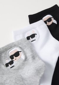 Tres pares de calcetines cortos en negro, blanco y gris que presentan diseños bordados de una persona de dibujos animados y un gato con gafas de sol.