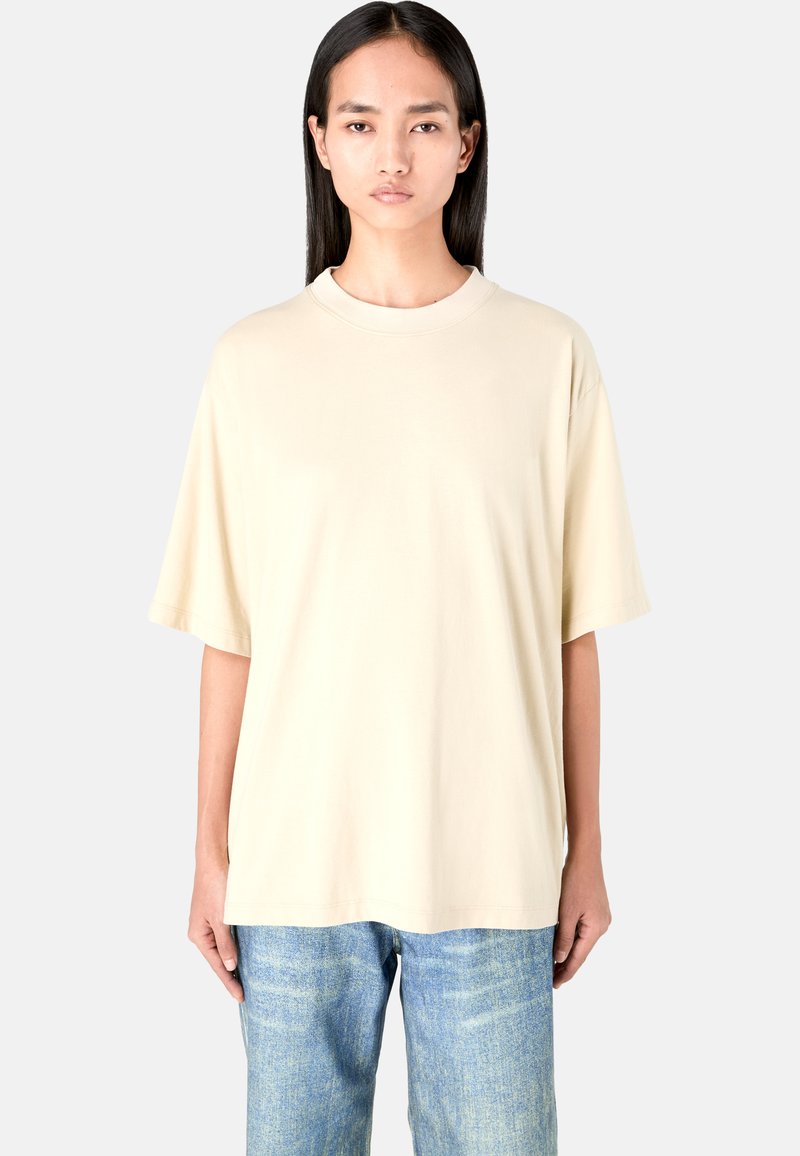 Beige oversized t-shirt in soft fabric with a crew neckline and short sleeves, paired with light blue slim-fit jeans.