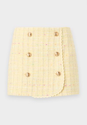 Žlutá tweedová sukně s texturovaným povrchem, dvouřadým zapínáním, zlatými knoflíky a zvlněným lemem. Vyznačuje se barevnými skvrnami po celém povrchu.