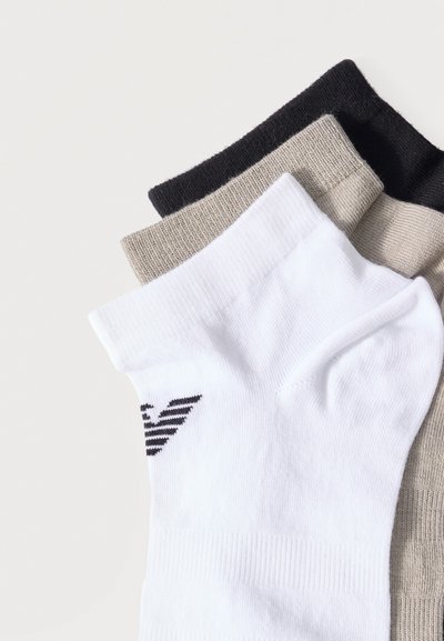 Τρία ζευγάρια κοντές κάλτσες σε λευκό, μπεζ και μαύρο στοιβαγμένα, με ένα μαύρο λογότυπο στο λευκό ζευγάρι κοντά στη μανσέτα.