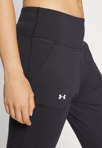 Černé sportovní legíny s vysokým páskem, hladkou texturou, bočními kapsami a malým bílým logem na stehně.