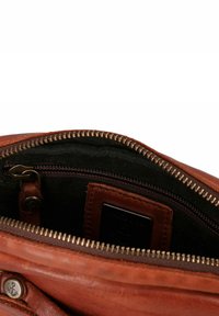 Brown leather bag interior featuring a dark fabric lining, a zippered pocket, and a metallic zipper. Anchor hardware detail visible.