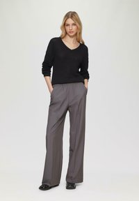 Maglione nero a maglia con scollo a V, abbinato a pantaloni grigi a vita alta e gamba larga e sandali neri decorati.