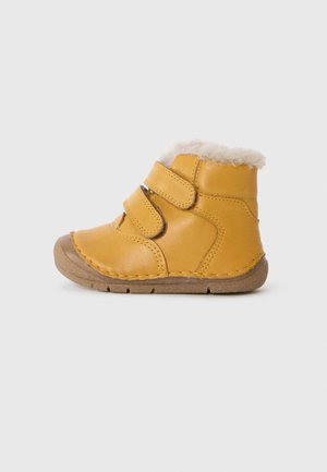 Botas de cano baixo em pele, amarelas, com duas fitas de Velcro, forradas com uma suave pelagem em creme e com sola de borracha. Detalhe cosido ao longo das bordas.