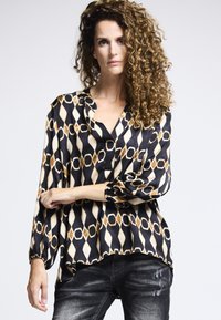 Schwarz-weiße gemusterte Bluse mit Diamant- und Kreisdesigns, langen Puffärmeln und einem lockeren Schnitt mit V-Ausschnitt.