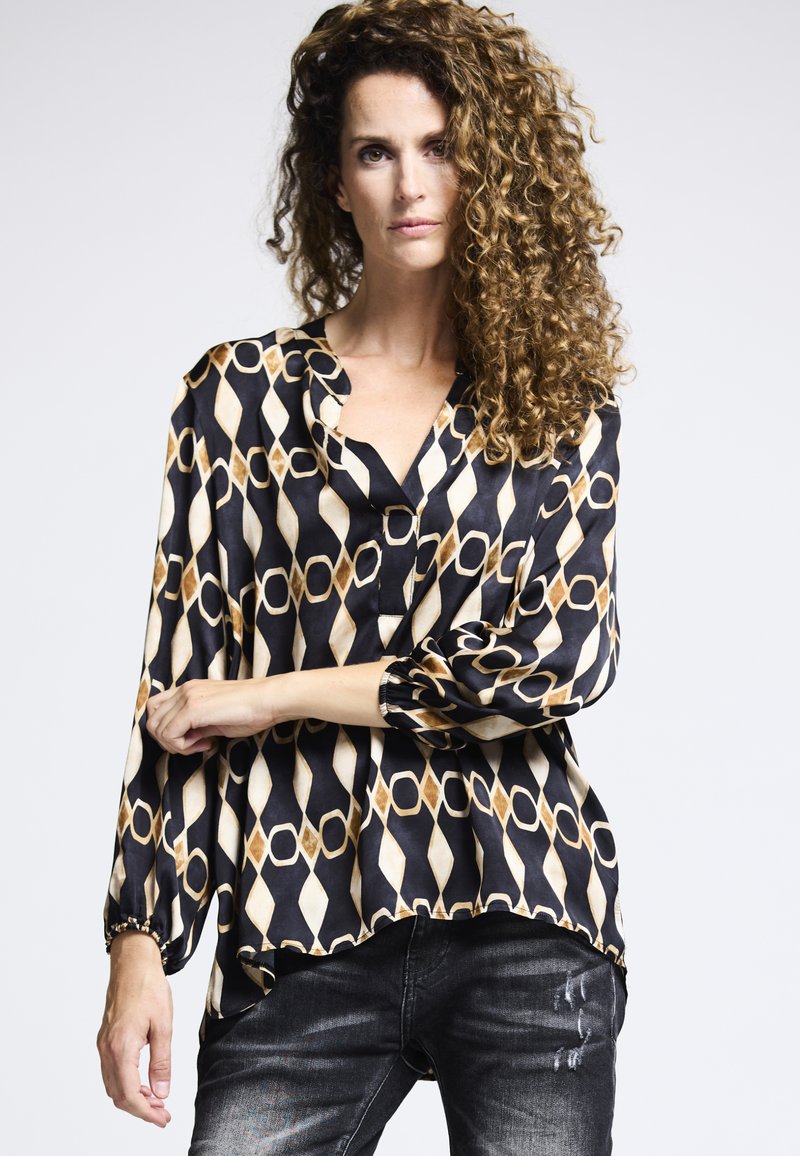 Schwarz-weiße gemusterte Bluse mit Diamant- und Kreisdesigns, langen Puffärmeln und einem lockeren Schnitt mit V-Ausschnitt.