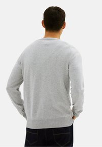 Grijze long-sleeve trui van zacht materiaal, met een ronde hals en geribde manchetten. De achterkant heeft een gladde textuur zonder patronen.