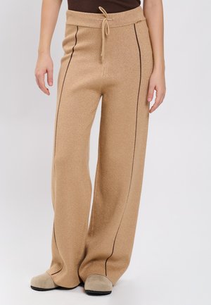 Beige bukser med vide ben og sorte lodrette sømlinjer, snøre i taljen, brugt med beige slip-on sko og en mørkebrun top.